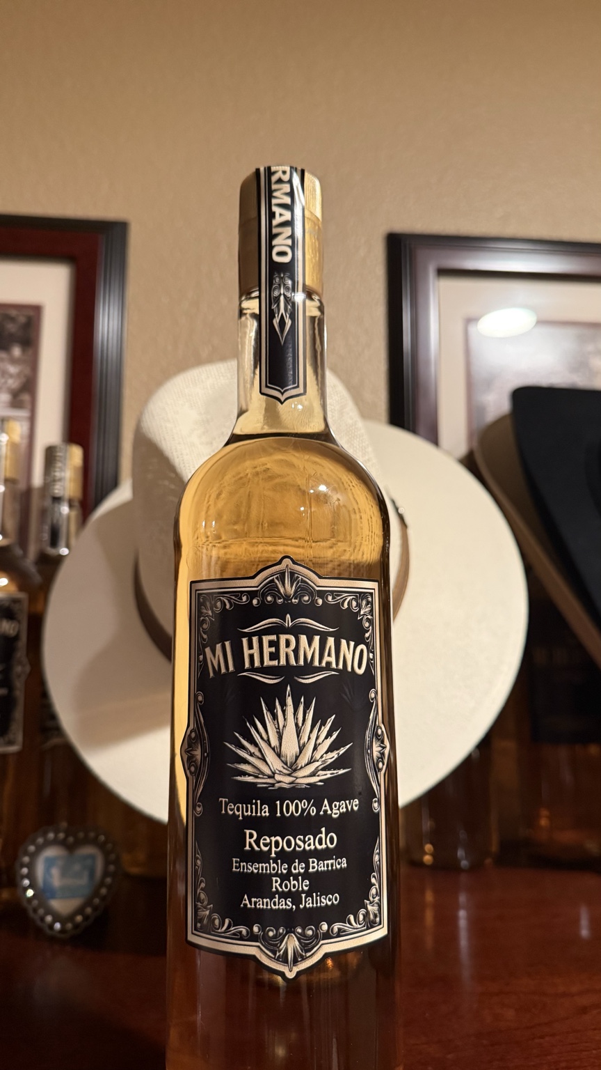Mi Hermano Reposado bottle with a black and gold agave label, photographed in front of a white cowboy hat